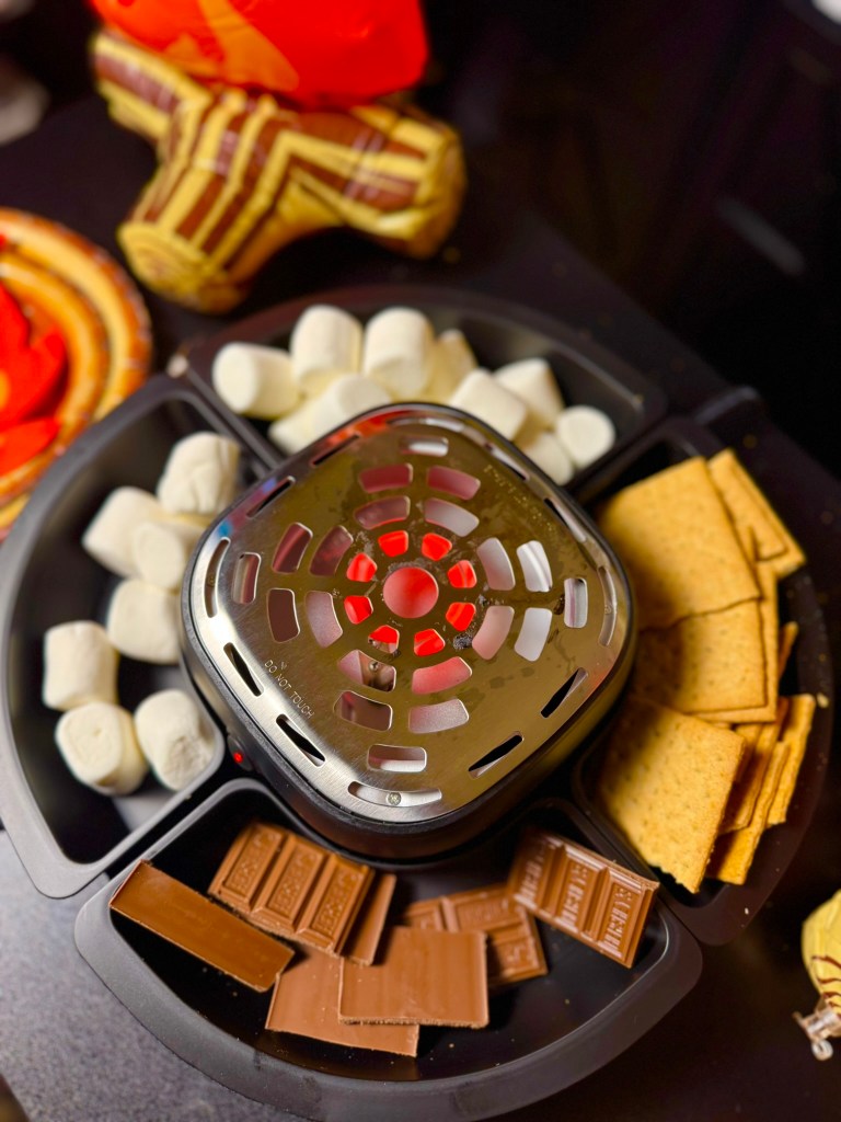 Camping birthday party s’mores station with marshmallows, graham crackers, chocolate, and an indoor s’mores maker.
