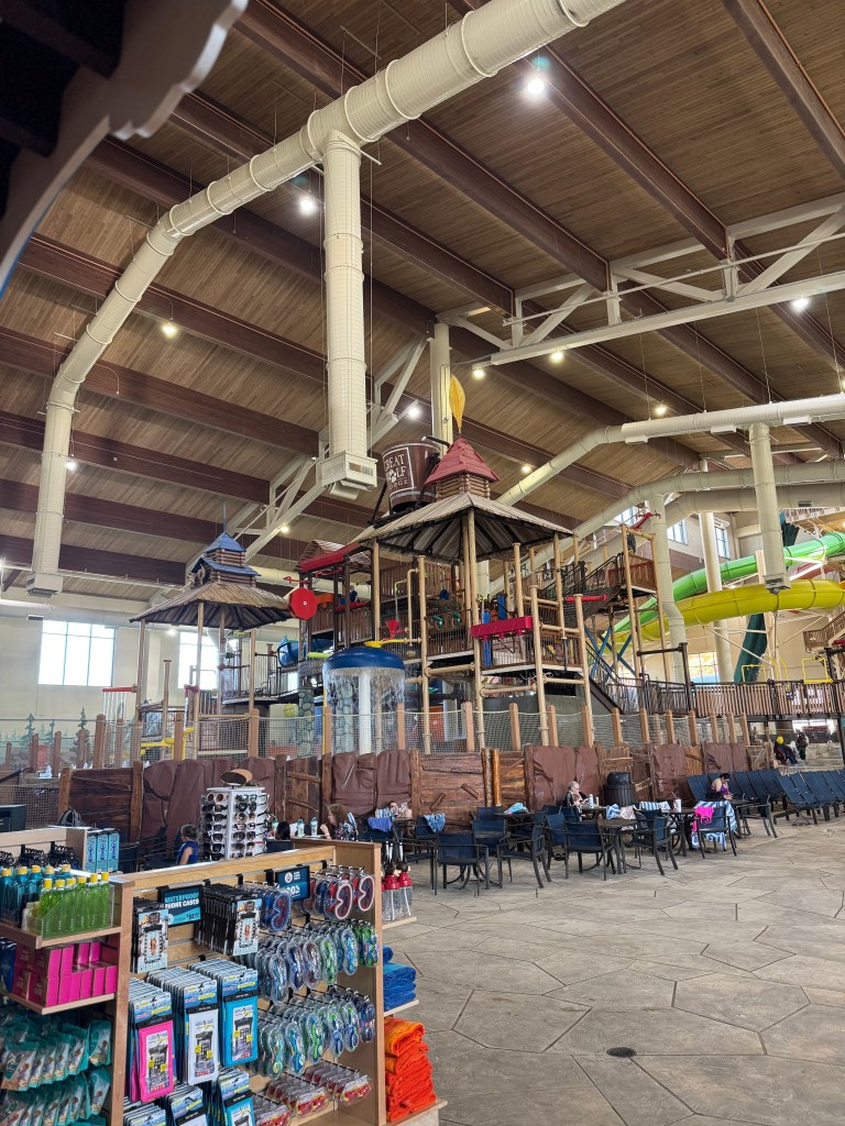 Interior view of the Great Wolf Lodge water park featuring a play area with slides and climbing structures, surrounded by seating, retail displays, and vibrant decor.