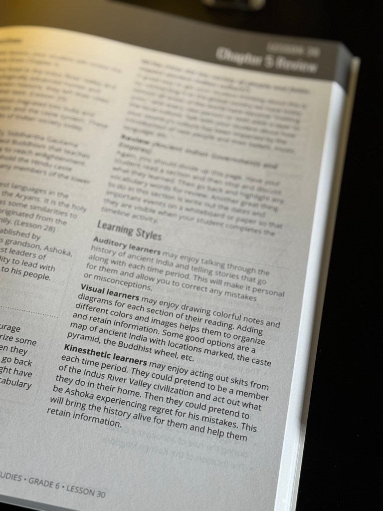 Close-up of an open social studies instructor's guide, displaying lesson information and learning styles tailored for visual, auditory, and kinesthetic learners.