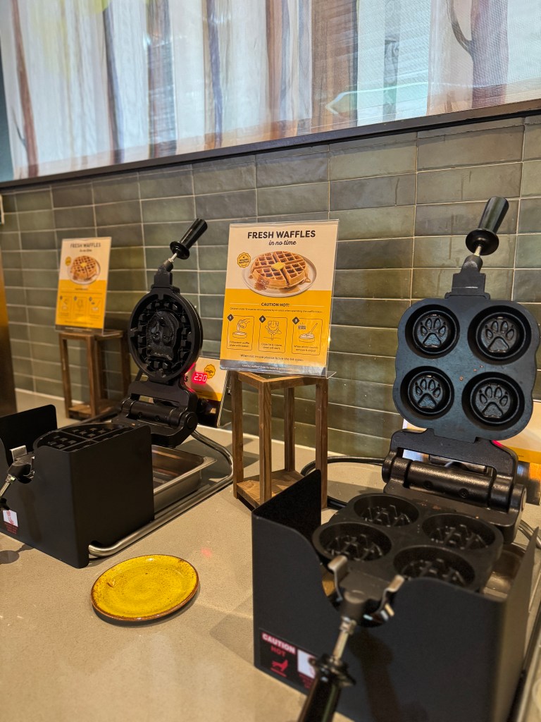 Display of waffle makers with paw print shapes and a sign indicating fresh waffles are available.