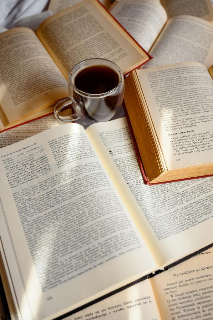 A cozy arrangement of open books with a clear glass cup of coffee in the center, creating an inviting reading atmosphere.