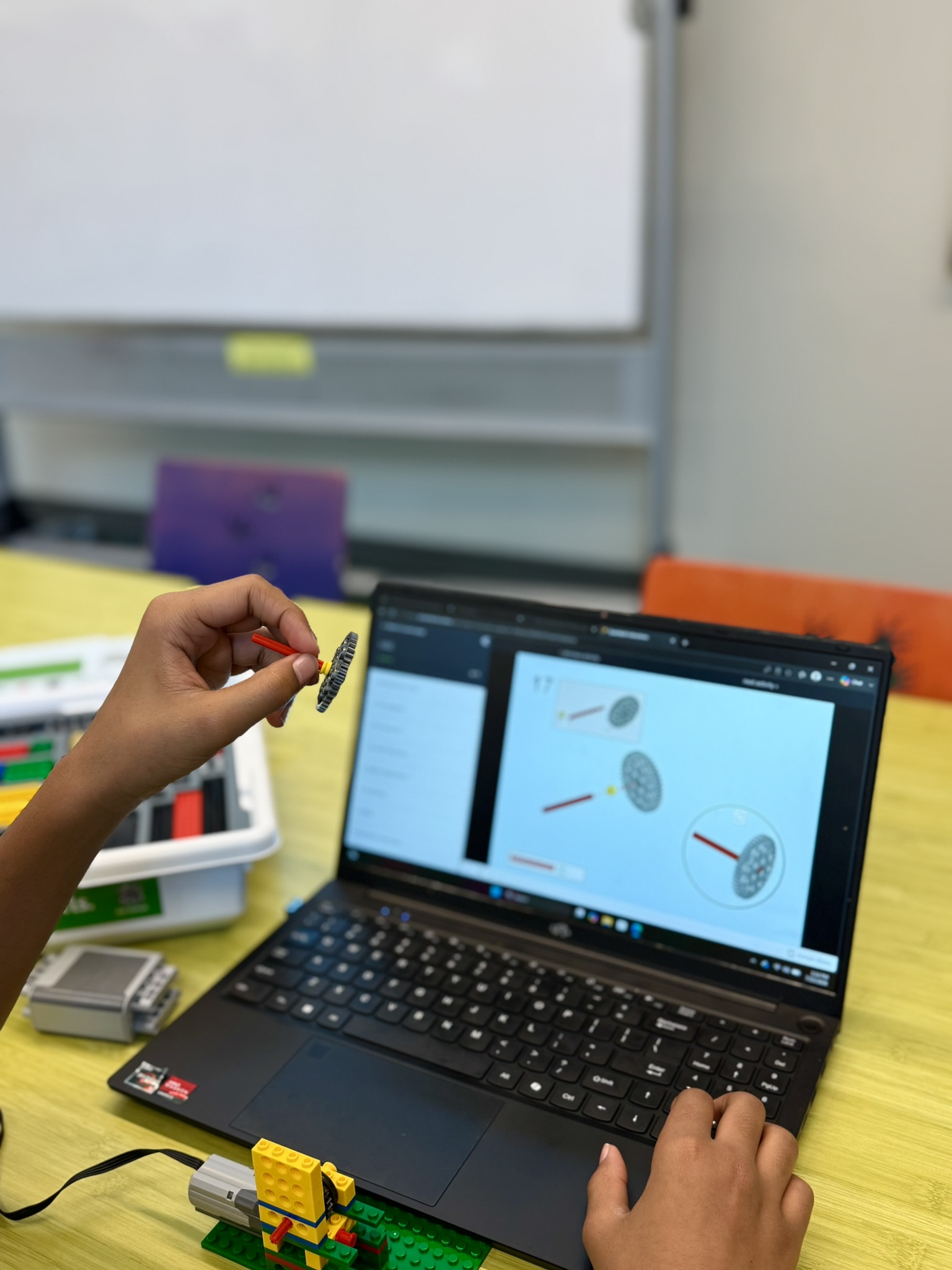 Hands assembling a LEGO gear piece while following instructions on a laptop screen