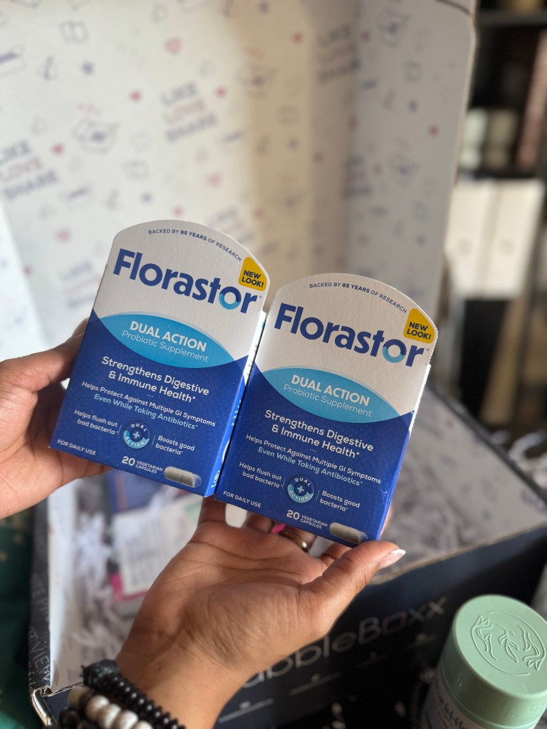 A person holding two boxes of Florastor Dual Action probiotic supplements with a branded backdrop.