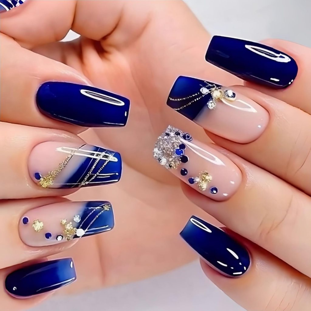 Glamorous navy blue square nails with glitter accents, rhinestones, gold foil, and glossy nude polish.