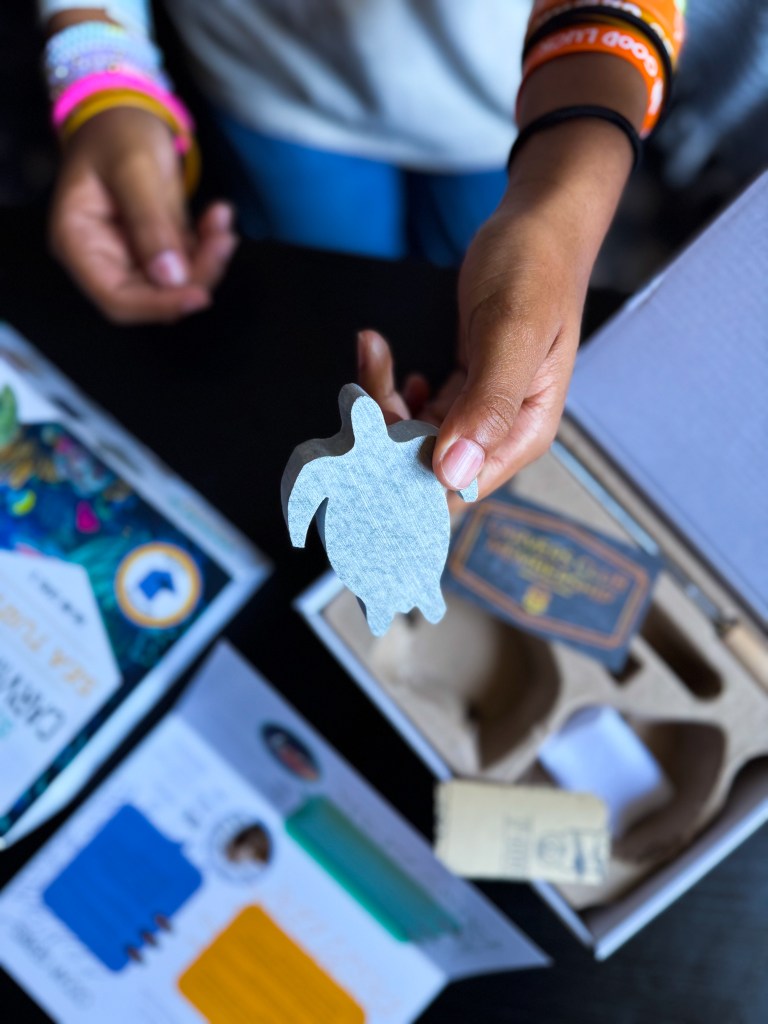 A child's hand holding a cut-out shape of a turtle, with colorful papers and a box displayed on a table.