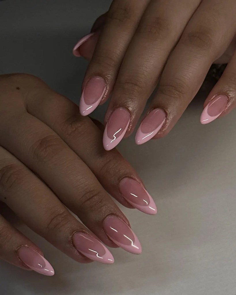 Close-up of two hands showing manicured long almond-shaped nails with a pink ombre design.