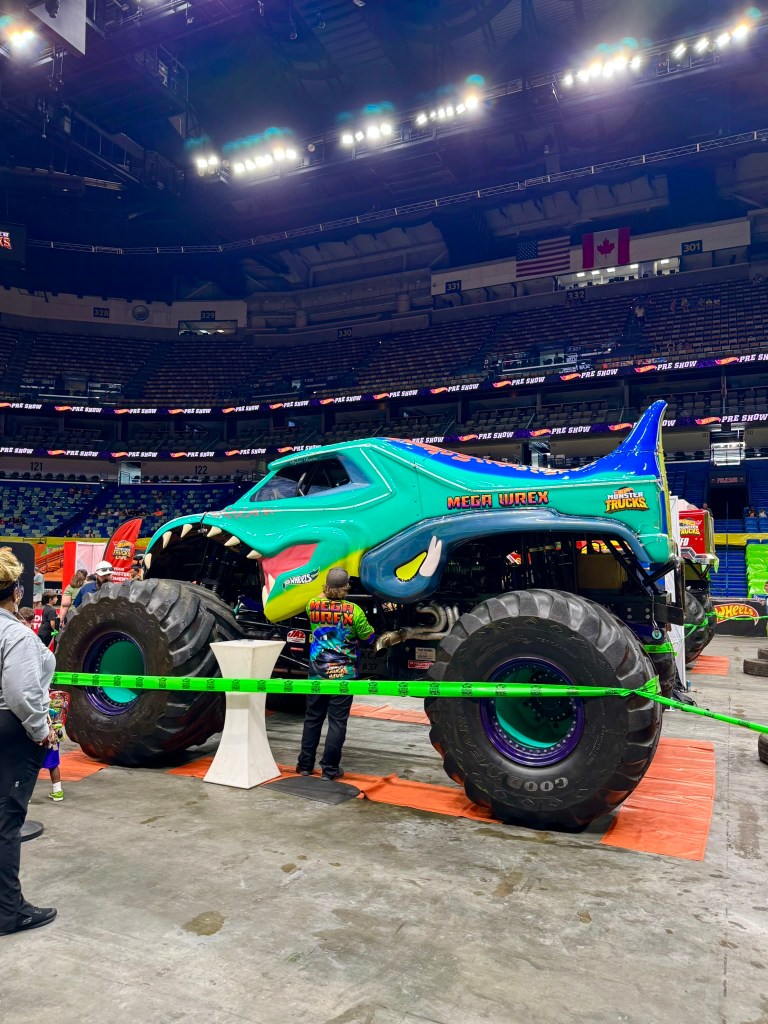 Full side view of the green and blue Mega Wrex monster truck on the arena floor.