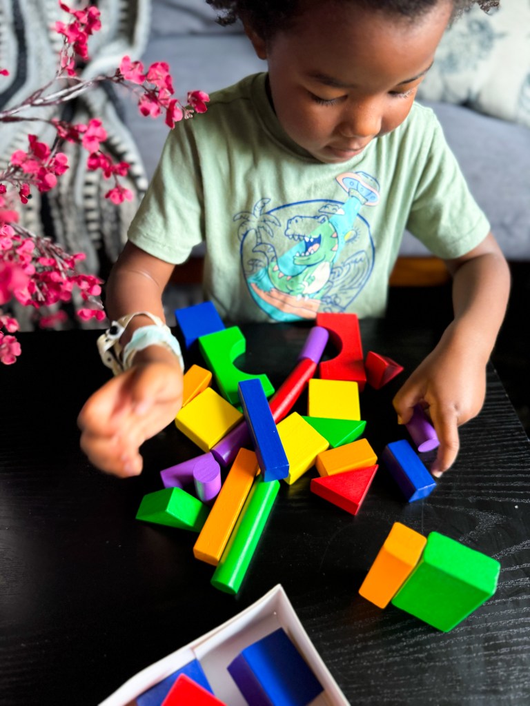 A young child playing with colorful building blocks on a table, surrounded by a floral decoration.