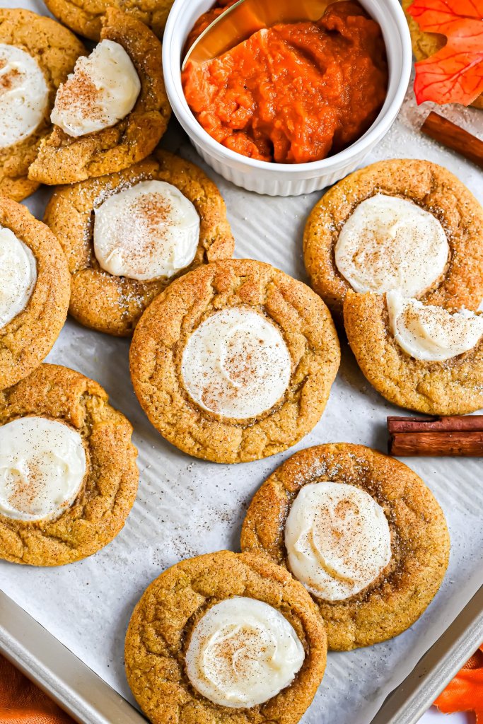 A tray of pumpkin cookies topped with cream cheese frosting and sprinkled with cinnamon, alongside a bowl of pumpkin puree.