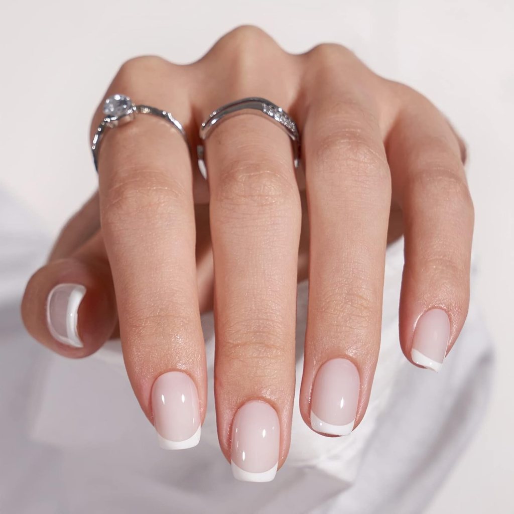 A close-up of a hand displaying well-manicured nails with a nude color and white tips, adorned with silver rings on two fingers.