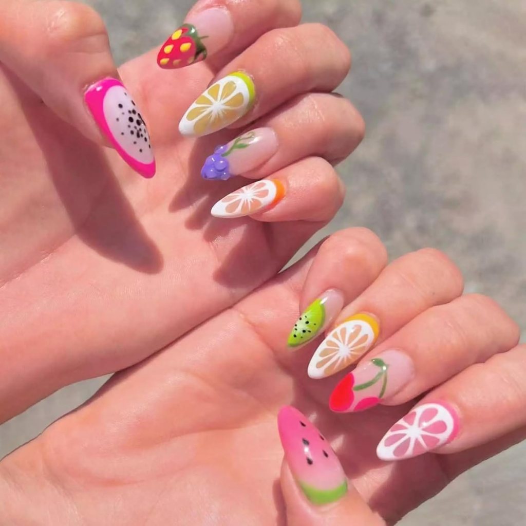Colorful and artistic manicure featuring various fruit designs, including strawberries, lemons, grapes, and watermelon, on long, pointed nails.