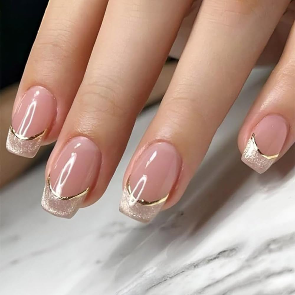 A close-up of manicured nails featuring a nude base color with glittery pink tips and gold accents in a chevron shape.