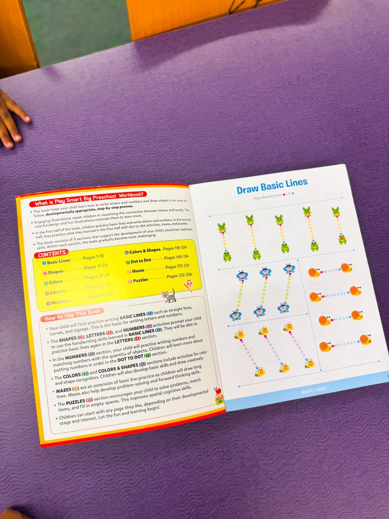 An open preschool workbook titled 'What is Play Smart Big Preschool Workbook?' with colorful illustrations and activities for tracing basic lines, letters, numbers, and shapes. The contents section includes pages on colors, mazes, and puzzles, with instructions for engaging children in developmental learning.