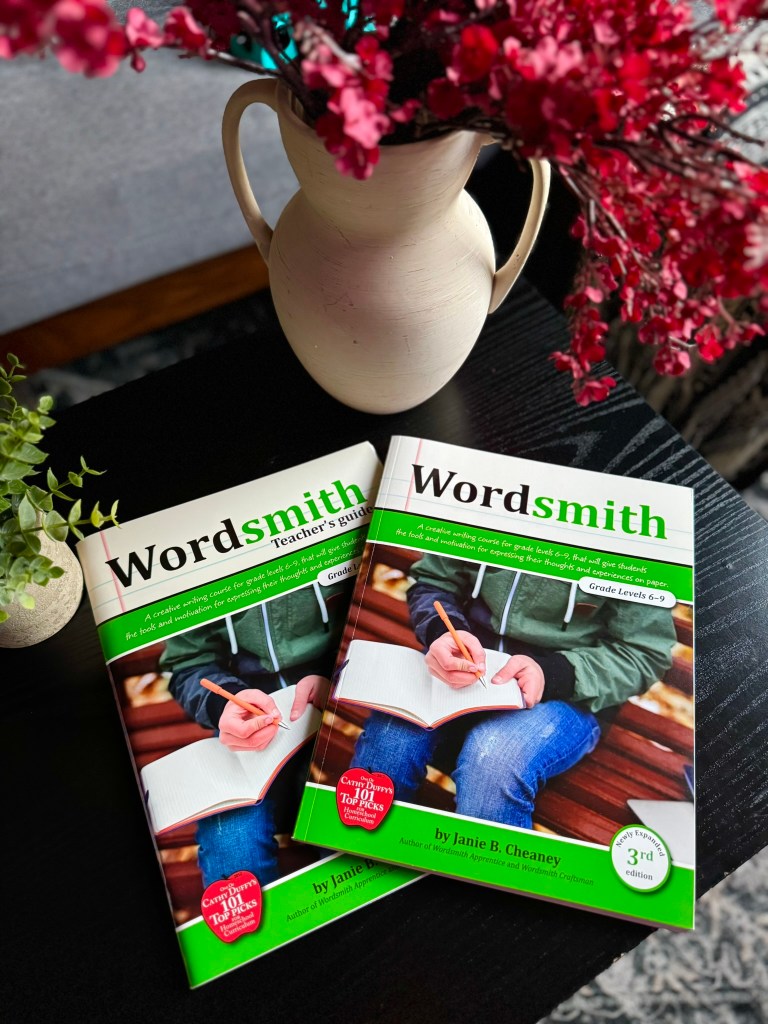 Two copies of the 'Wordsmith Teacher's Guide' book by Janie B. Cheaney on a table, accompanied by a vase of flowers.