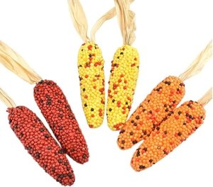 Colorful decorative corn cobs in shades of red, yellow, and orange, surrounded by dried husks, perfect for Thanksgiving decor.
