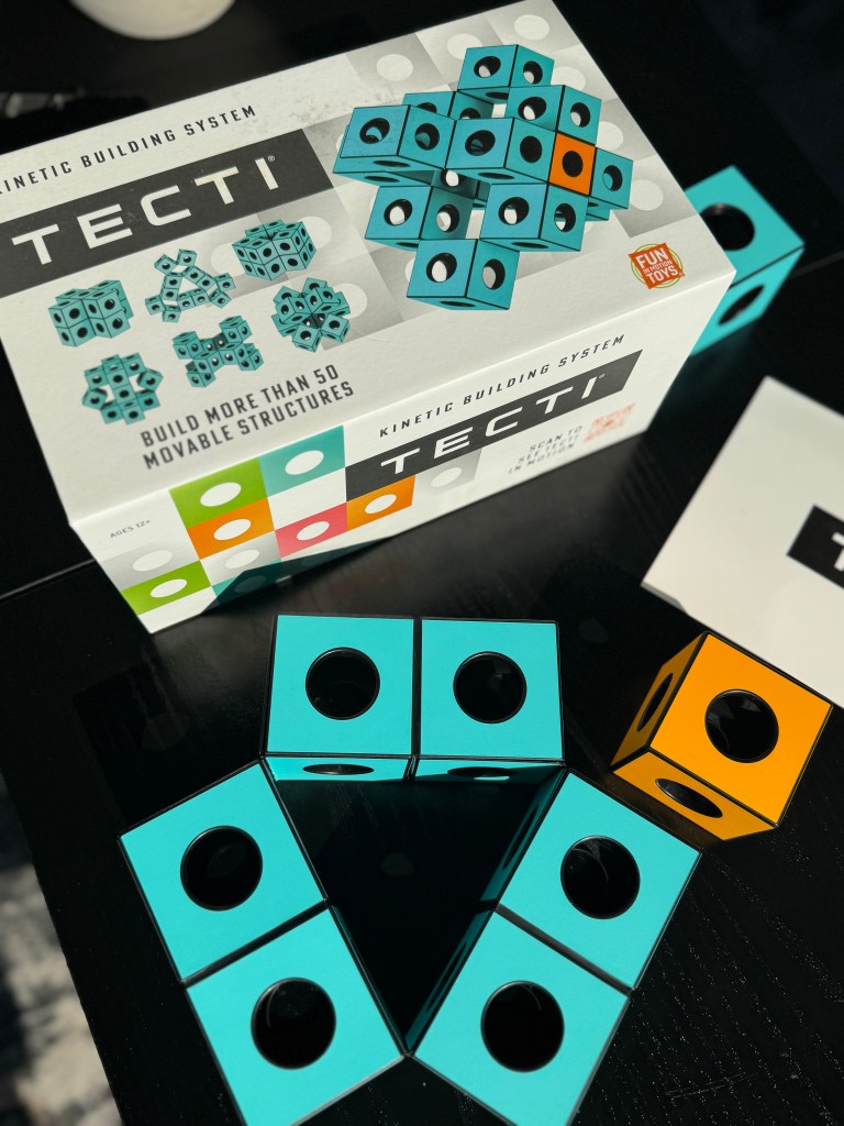 A colorful Tecti kinetic building system box with turquoise and black cubes displayed on a dark surface, showcasing the product's branding and features.
