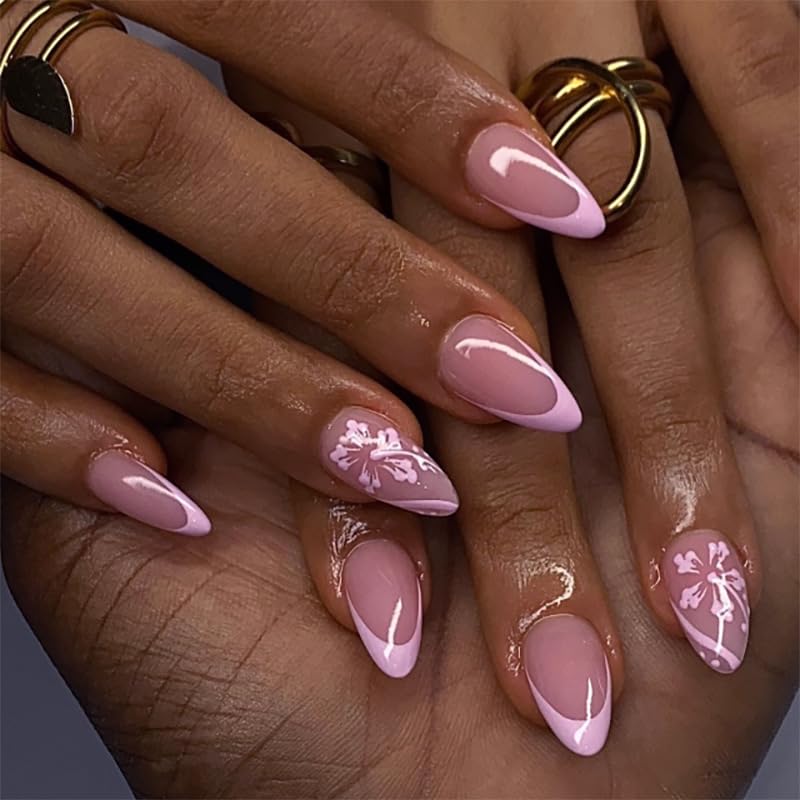 Close-up of hands displaying manicured nails with a light pink polish and floral designs, featuring gold rings on fingers.