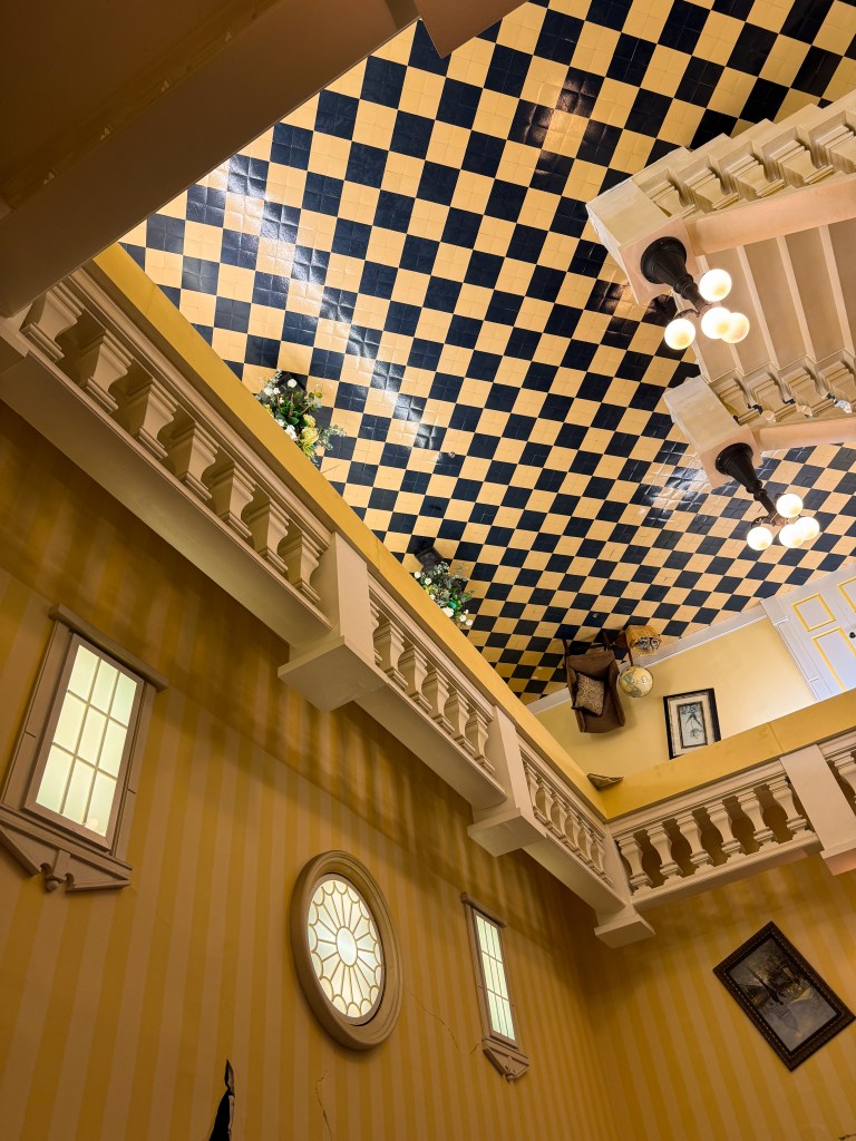 View of an indoor space with a checkered ceiling in yellow and blue, featuring decorative flowers, light fixtures, and wall accents.