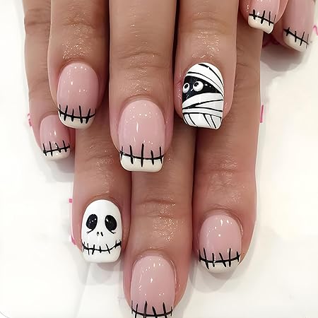 Nail design featuring a playful Halloween theme with a mummy accent, skulls, and stitched tips on nude-colored nails.