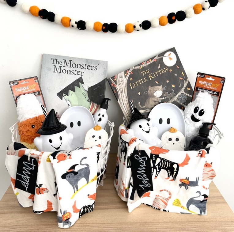 Two coordinating Halloween-themed baskets filled with plush ghost toys, storybooks, and decorations, placed on a wooden surface.