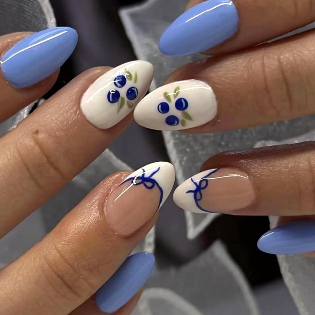 Close-up of hands showing manicured nails with a blue and white color scheme, featuring floral and bow designs.