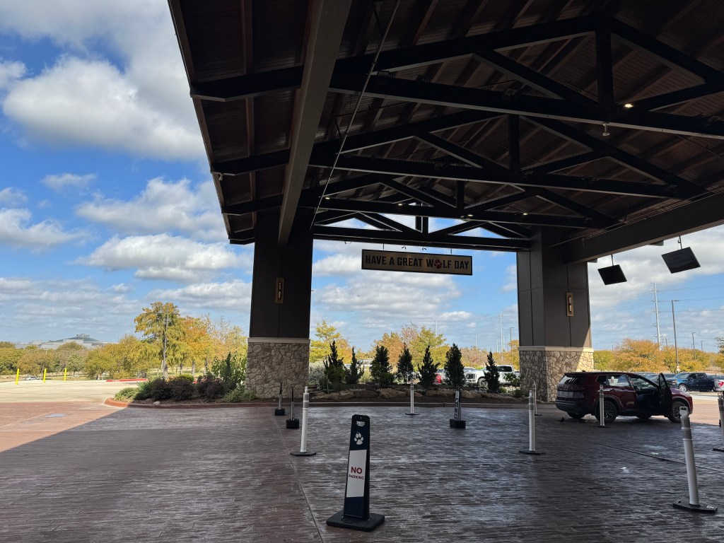 Exterior view of the Great Wolf Lodge entrance with a sign reading 'HAVE A GREAT WOLF DAY' and a clear sky with scattered clouds.