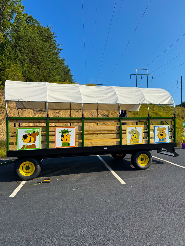 A colorful wagon with cartoon character paintings on the sides, parked in a lot under a clear blue sky.