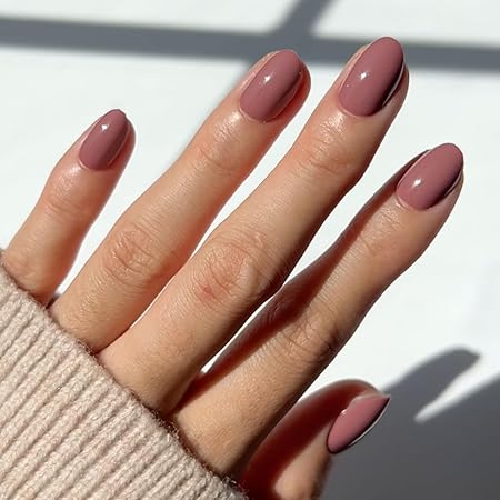 A close-up of a hand displaying elegantly manicured nails in a soft mauve color, showcasing a stylish and modern look, with a cozy sweater in the background.