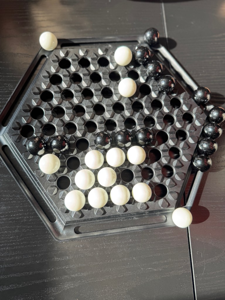 Close-up of an Abalone game board featuring a hexagonal grid with black and white marbles positioned strategically within the holes.