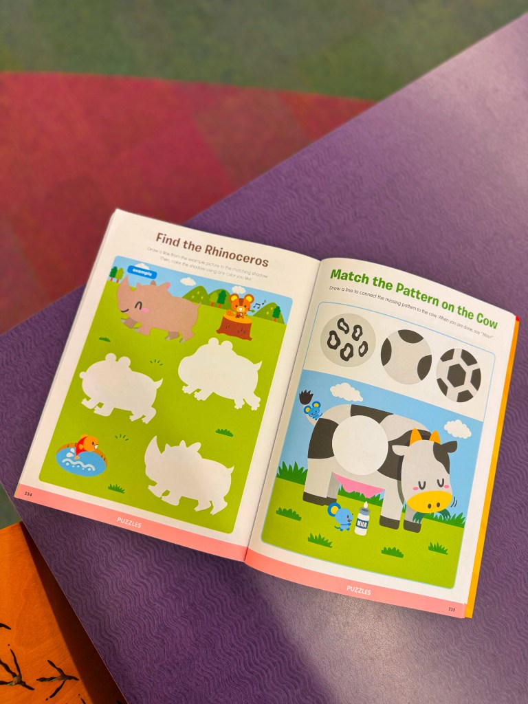 An open children's activity book featuring two puzzle pages. The left page asks to 'Find the Rhinoceros' among several animal silhouettes on a green background. The right page features 'Match the Pattern on the Cow' with images of a cow and various patterns.