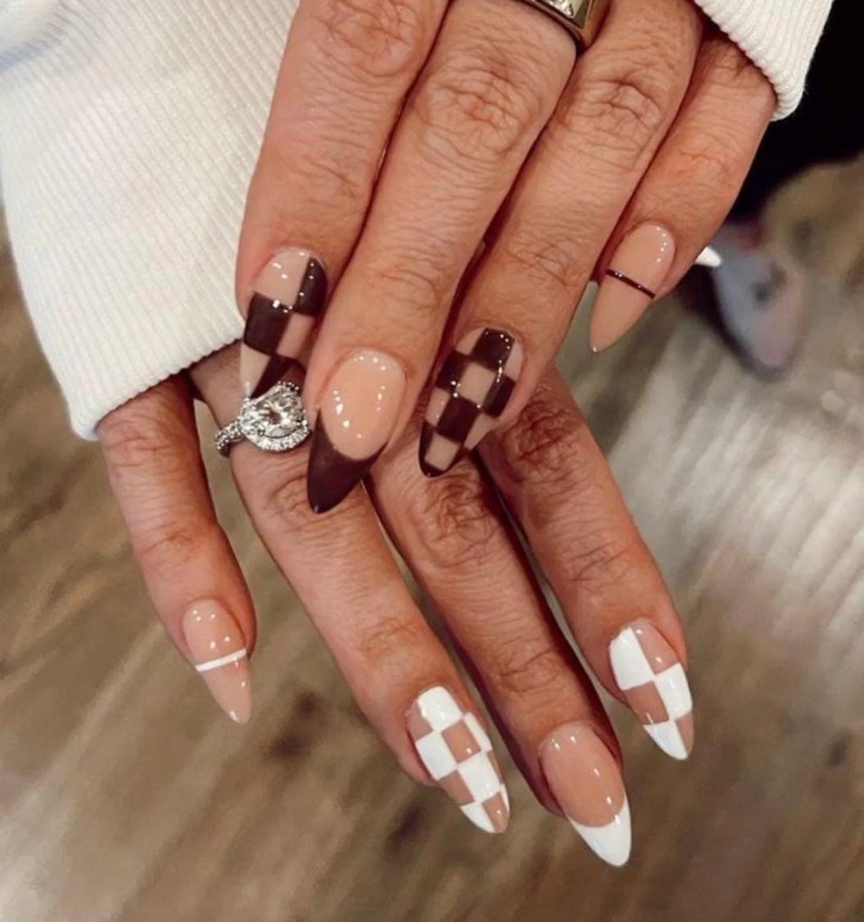 Close-up of hands showcasing festive Thanksgiving nail art featuring a mix of checkered, solid, and patterned designs in earthy tones like brown, beige, and white.