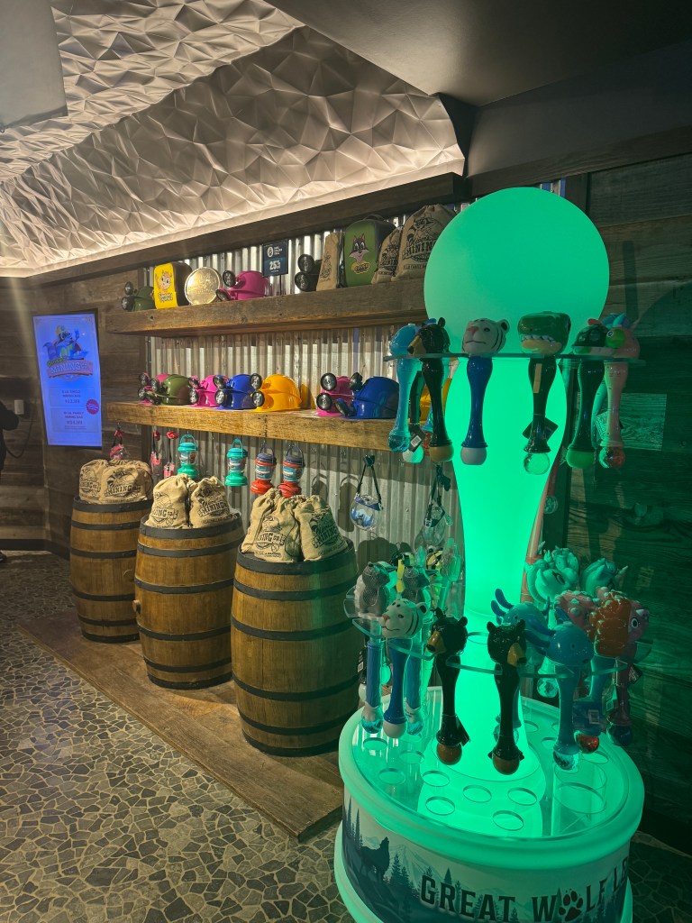 A display of colorful interactive wands and themed merchandise at Great Wolf Lodge, featuring decorative barrels and a softly glowing light installation in the background.