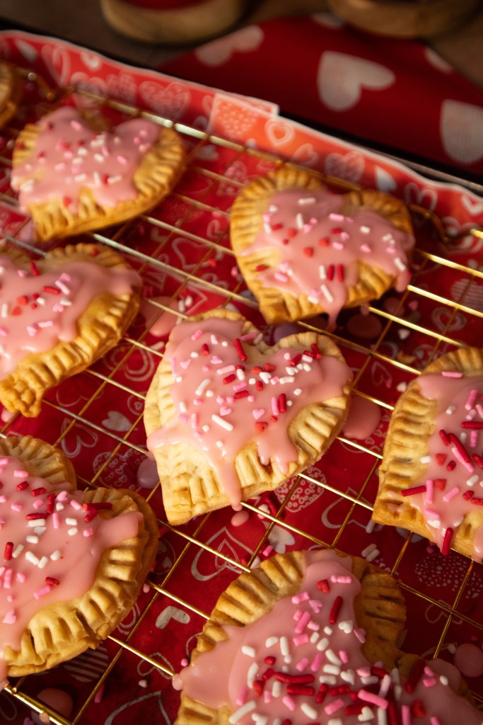 A tray of heart-shaped pop tarts topped with pink icing and colorful sprinkles.