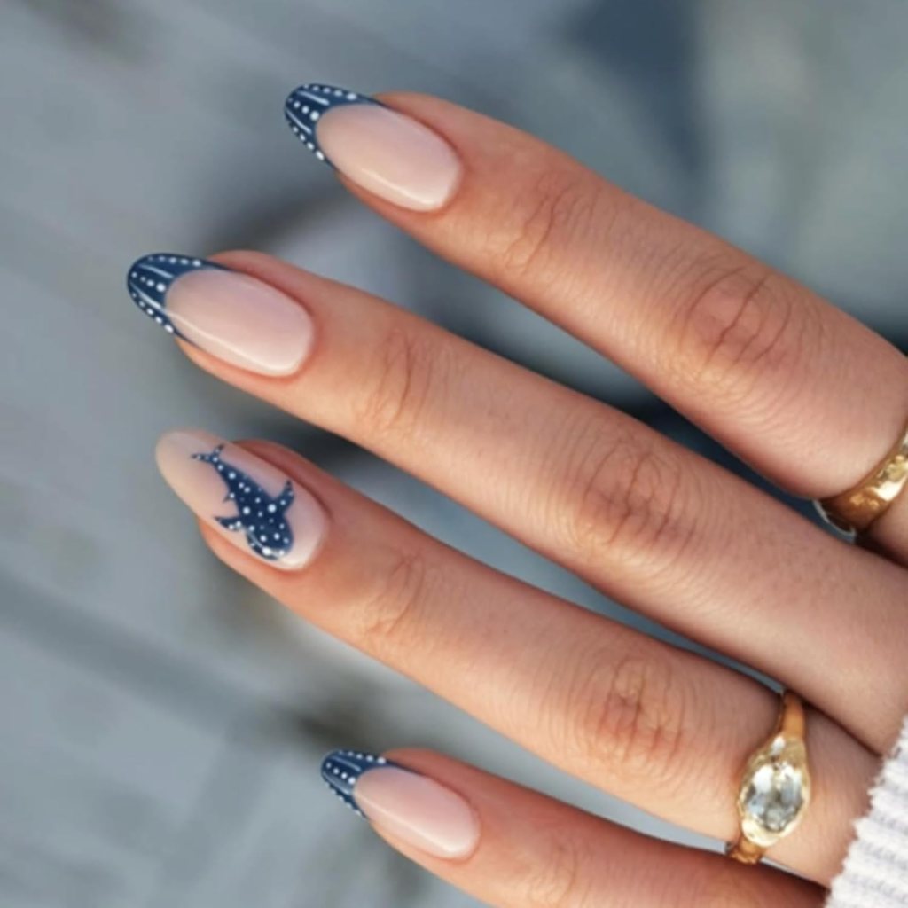 Nude almond nails with navy blue dotted French tips and whale shark accent nail art.