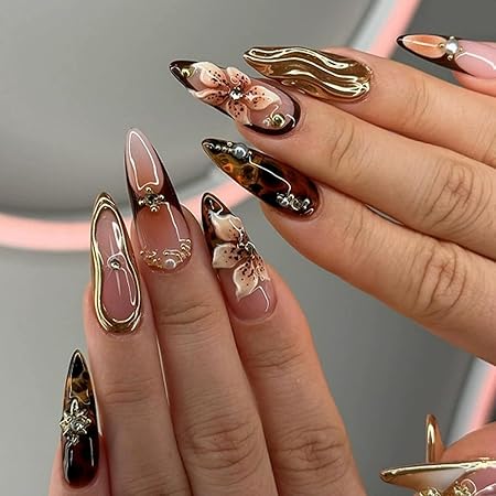 A close-up of elegantly designed nails featuring a mix of glossy and matte finishes, ornate floral patterns, and gold embellishments. The nails are displayed in a striking arrangement, showcasing a blend of natural and artistic elements.