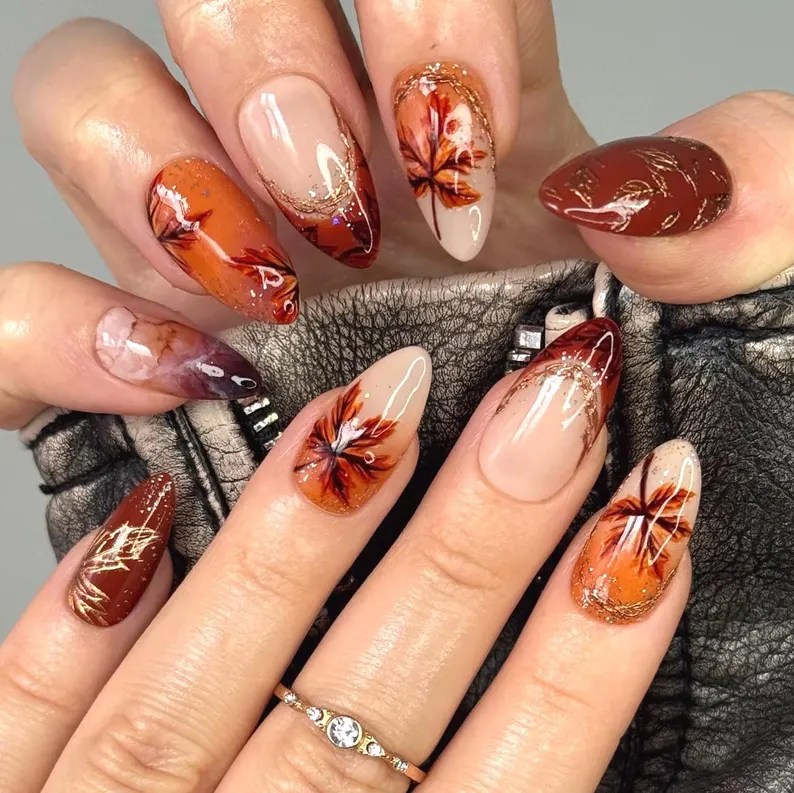 Elegant autumn nail design featuring burnt orange and chocolate tones with decorative leaf accents and gold glitter.