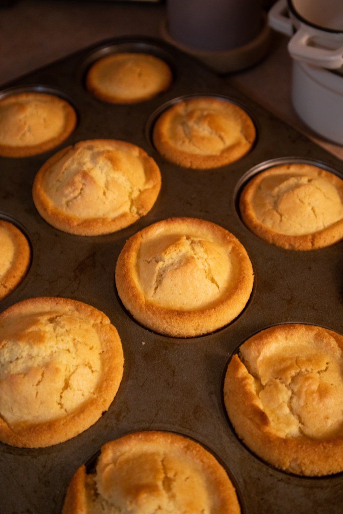 Freshly baked muffins in a metal muffin tin, golden brown with a light crust.