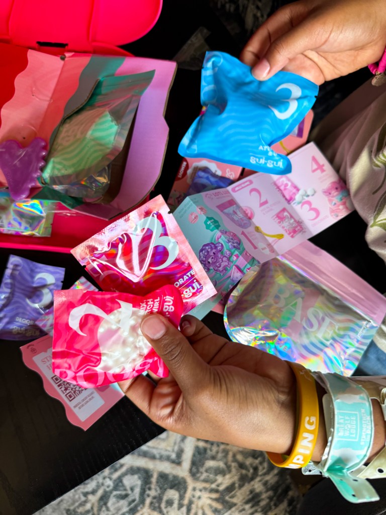 A person holding colorful packaging with various designs, including pink and blue, while a box filled with more packaging is in the background.