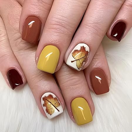 Close-up of manicured nails featuring autumn-inspired colors: rich burgundy, warm brown, and a vibrant yellow with hand-painted fall leaves on a white accent nail.