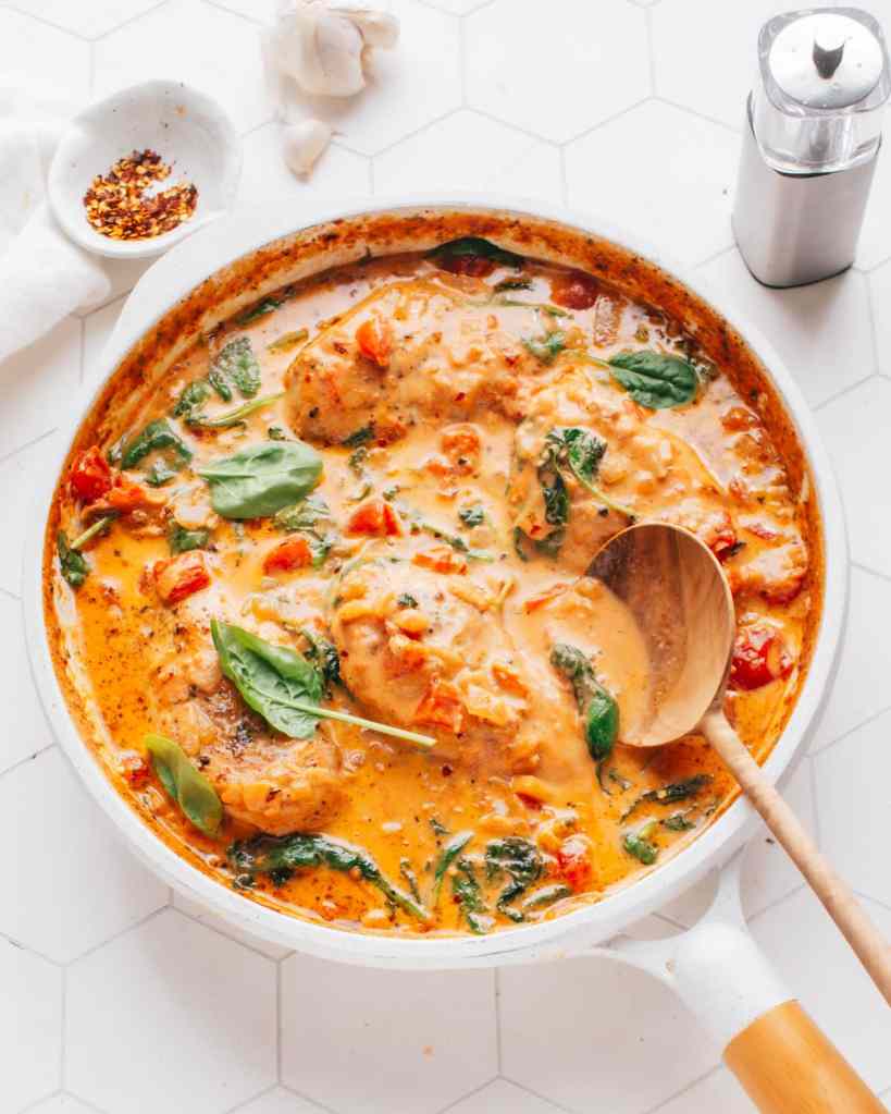 A creamy garlic chicken dish with tender chicken breasts simmered in a rich sauce featuring tomatoes and spinach, garnished with fresh basil.