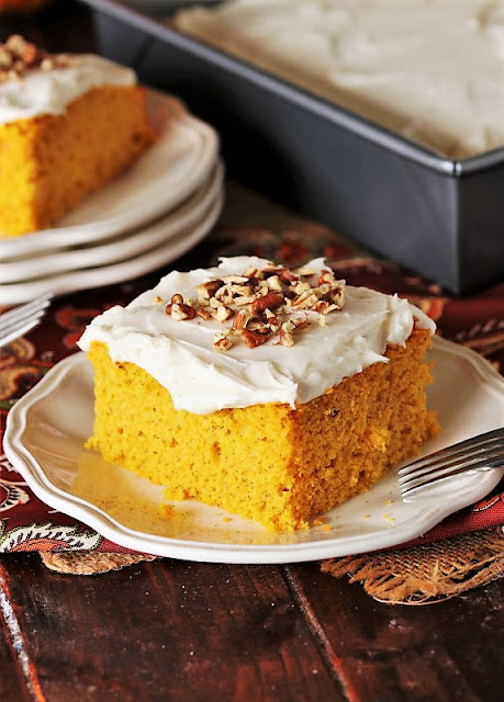 A slice of moist pumpkin cake topped with cream cheese frosting and chopped pecans, served on a decorative plate.