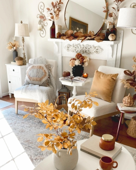 A cozy living room corner decorated for fall, featuring soft armchairs, a rustic coffee table, autumn foliage accents, and candlelight, creating a warm and inviting atmosphere.