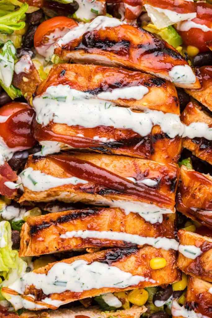 Sliced grilled chicken breast topped with barbecue sauce and ranch dressing, served on a bed of fresh greens, tomatoes, and corn.