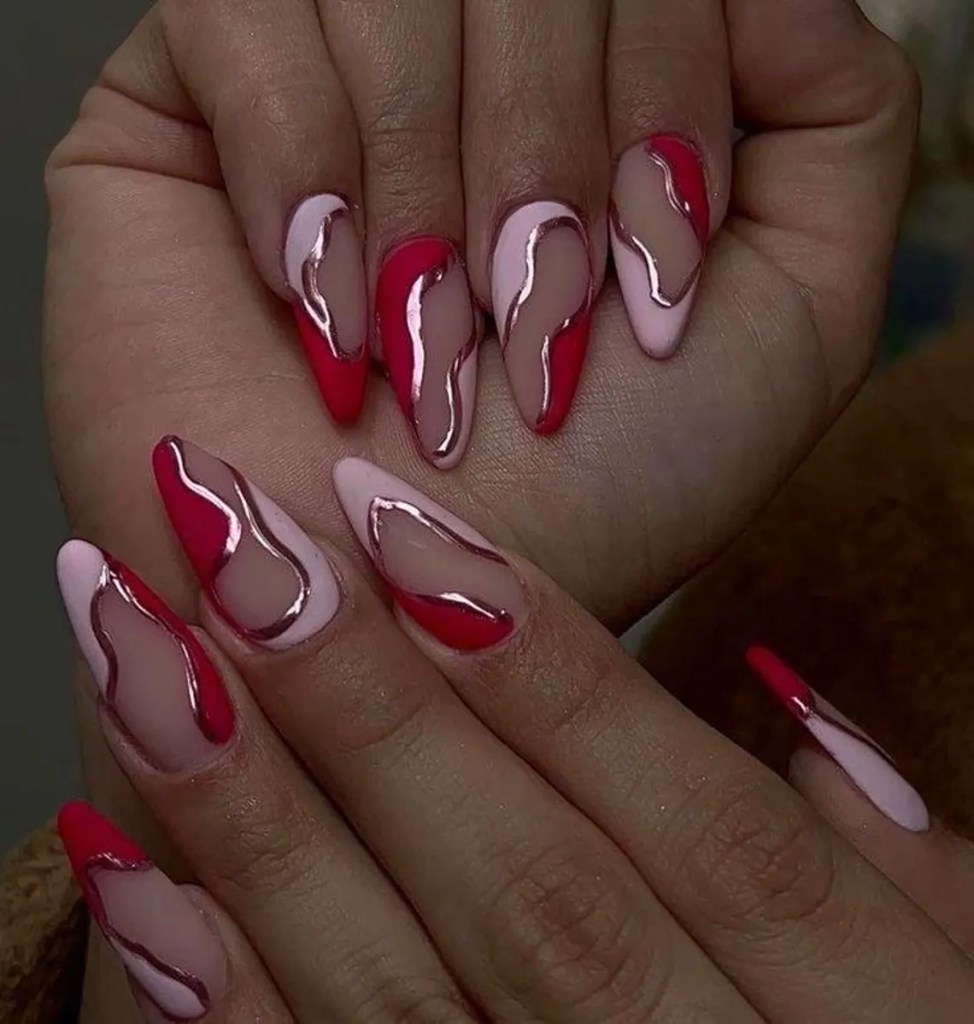 Close-up of hands displaying a stylish manicure featuring elongated nails with a design that includes alternating sections of pink and red colors, accented by flowing lines and glossy finishes.