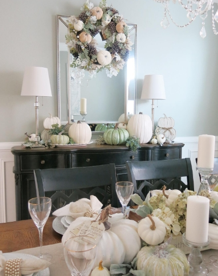 A beautifully styled fall dining table with white and green pumpkins, a decorative wreath, and elegant tableware, creating a warm and inviting atmosphere.