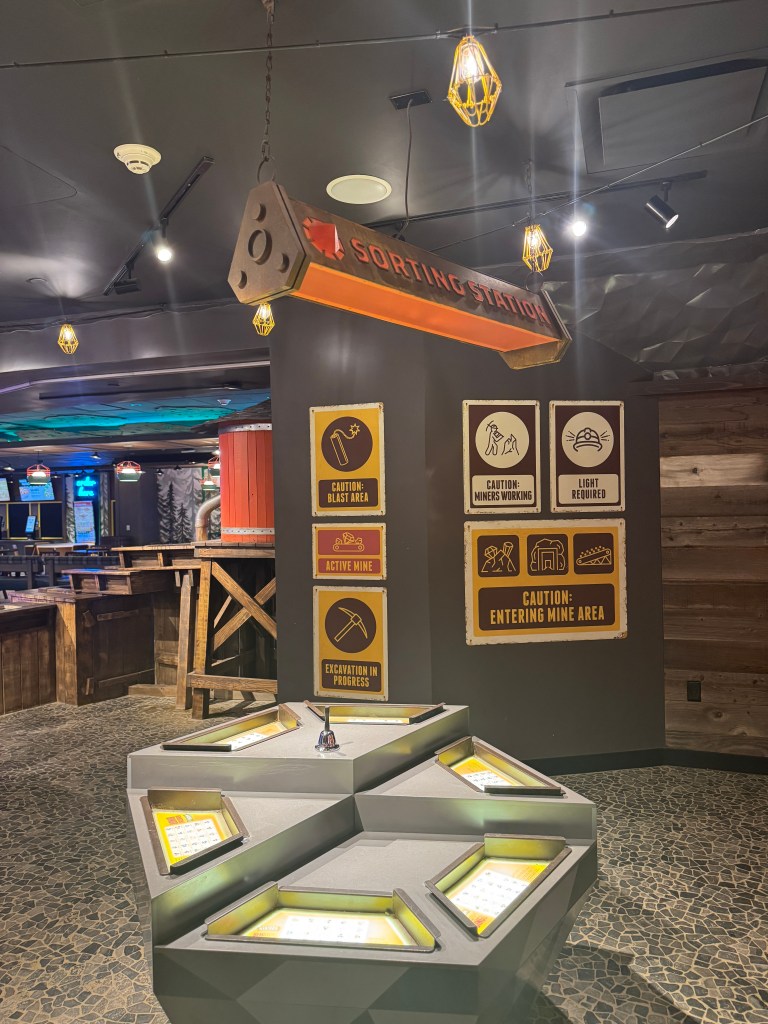 Indoor sorting station at Great Wolf Lodge, featuring signs for caution, active mine, and excavation in progress, with illuminated sorting trays.