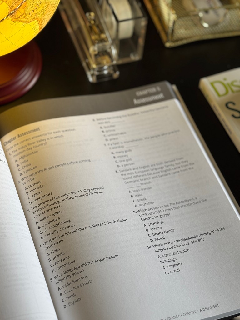 An open book displaying a chapter assessment for a social studies curriculum, with a globe partially visible in the background.
