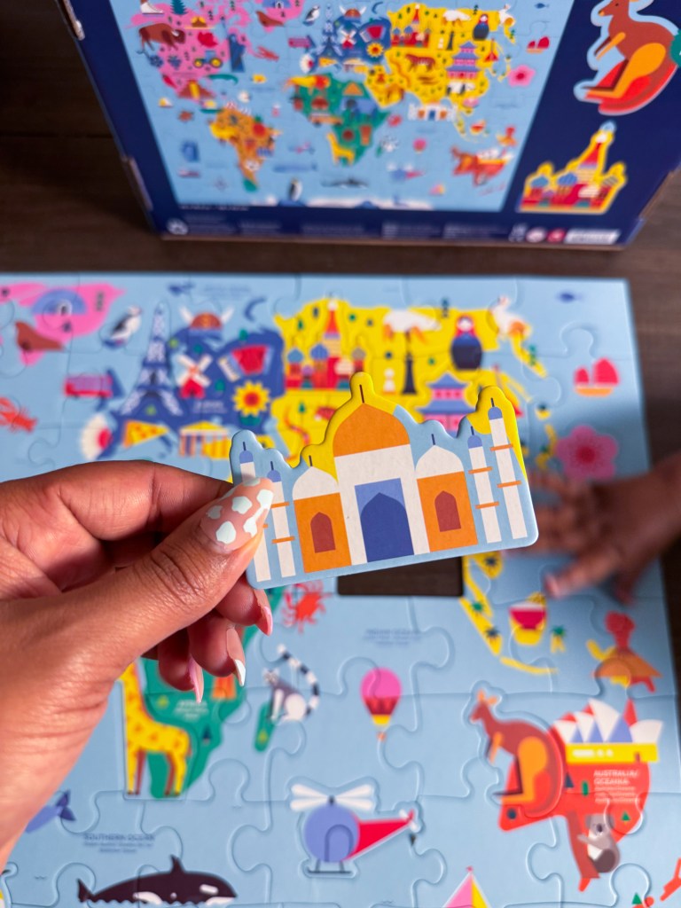 Hand holding the Taj Mahal puzzle piece above the completed world map geography puzzle.