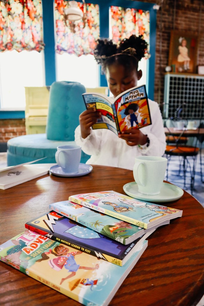 Young girl smiling while reading a Mia Mayhem chapter book inside a colorful reading space.