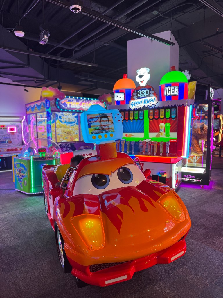 Kids ride-on racing game inside Northern Lights Arcade at Great Wolf Lodge Grapevine with colorful arcade machines in the background.